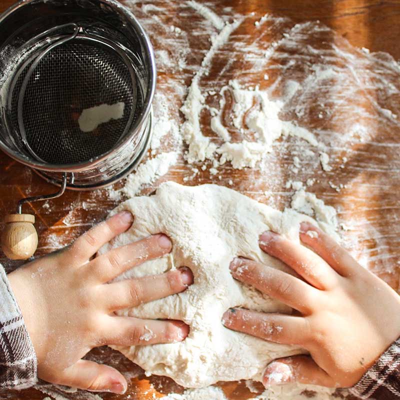 Young hands making bread on a wooden table.