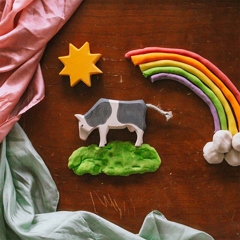 Rainbow play dough next to a wooden cow