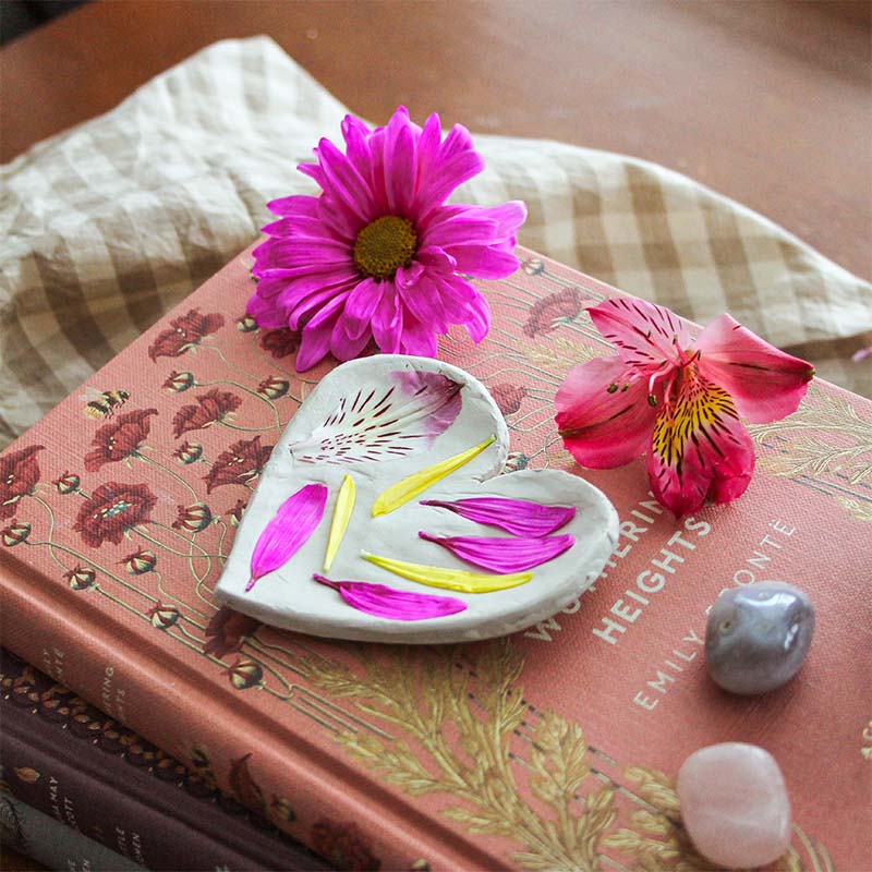 A clay trinket dish sits on a pink book with flowers.