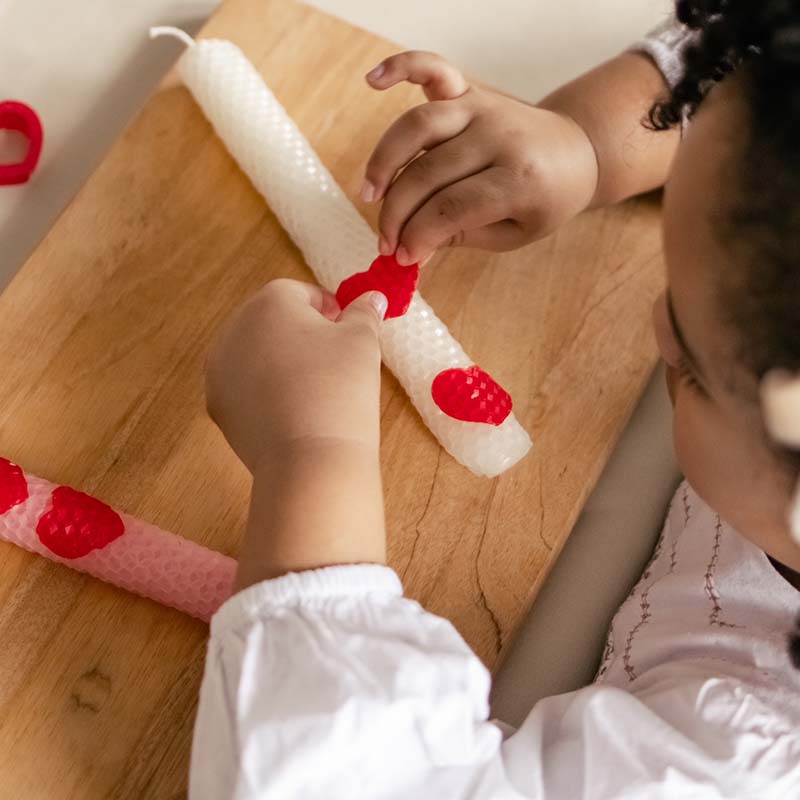 A young girl is decorating Valentine's Day candles.