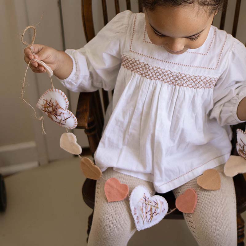 A young girl is holding an embroidered heart garland.