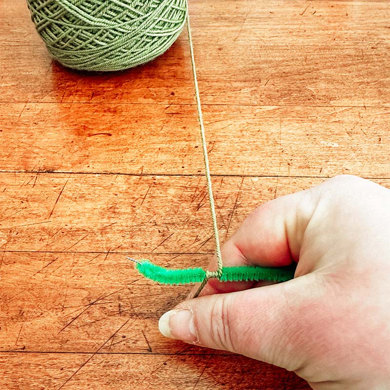 A pipe cleaner being wrapped in a yarn diy craft