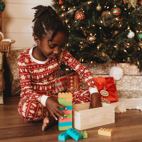 Child plays with colorful wooden interlocking blocks, similar to duplo, she has them stacked into a tower and is pulling more out of a wood box