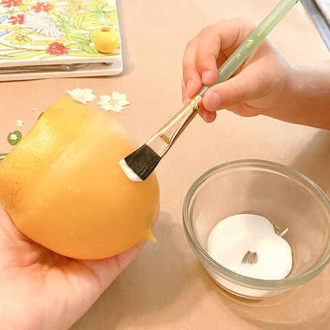 A child brushes glue onto the beeswax luminary.