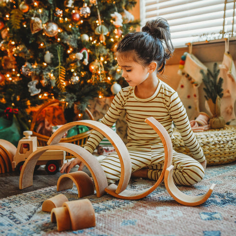 Child builds with grimm's 12 piece natural rainbow stacking arches in front of christmas tree