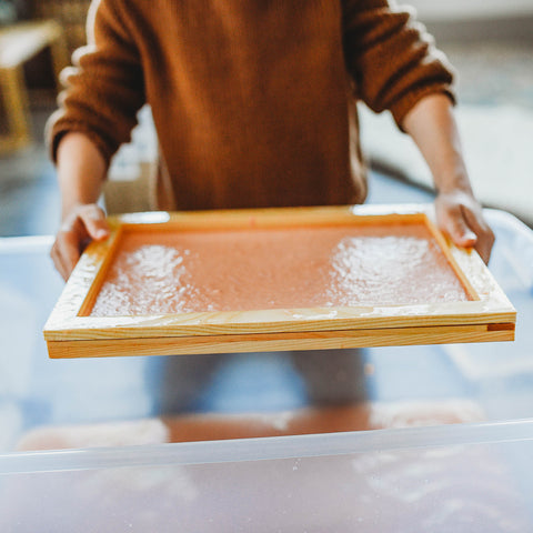 A child dipping screen into paper pulp to make recycled paper.