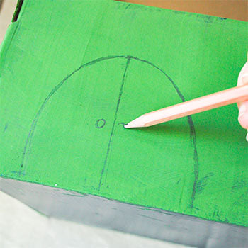 A pencil is drawing the doors on a green painted shoebox.