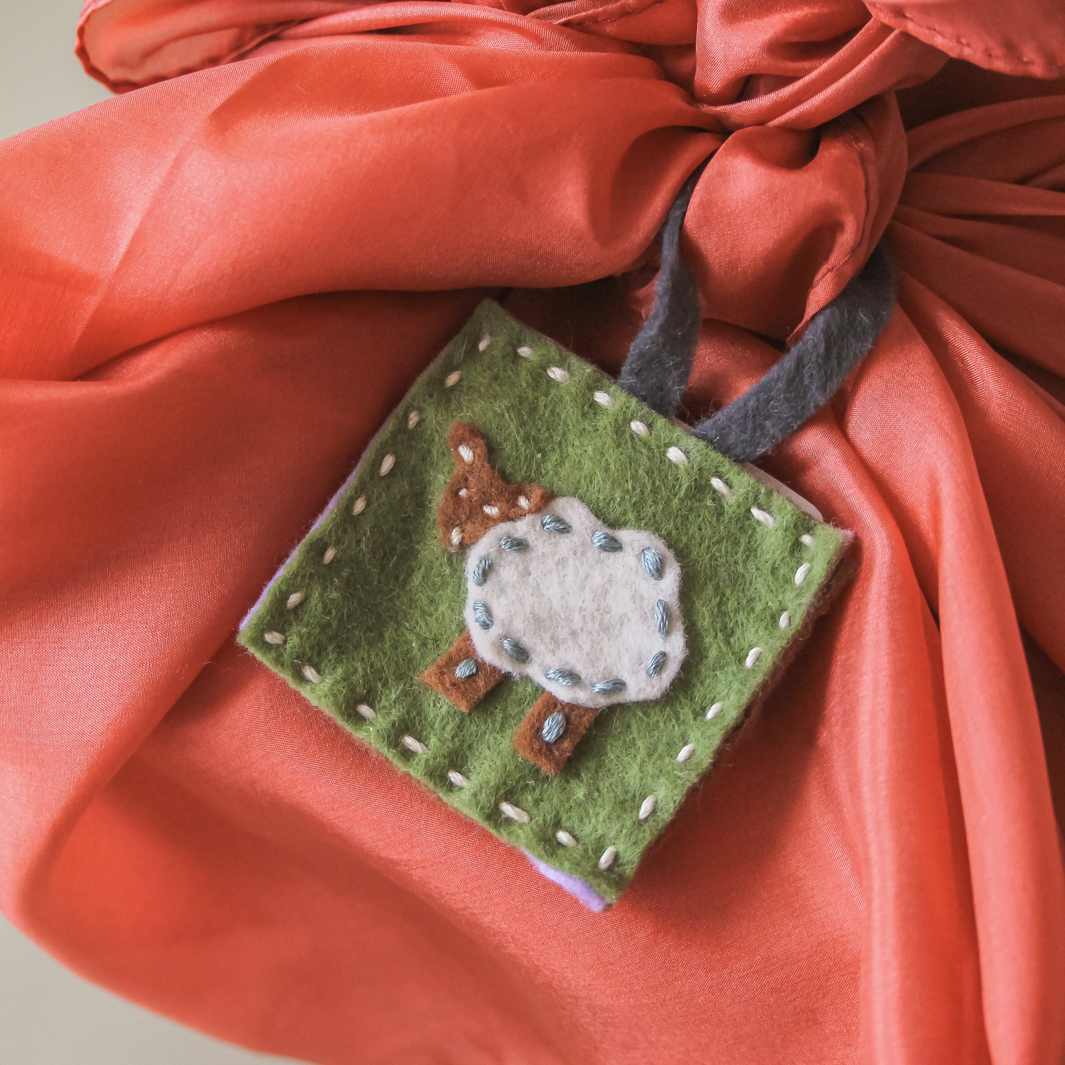 A felted sheep tag sits on a playsilk wrapped gift box.