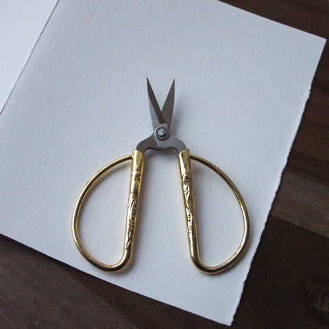 Gold scissors sit on a piece of paper.