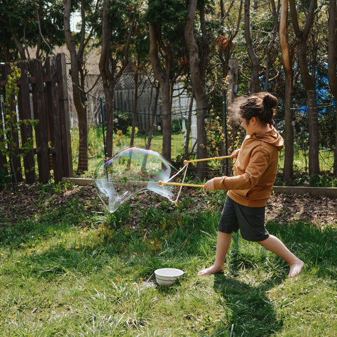 Child blowing a large far out bubble with wooden wands