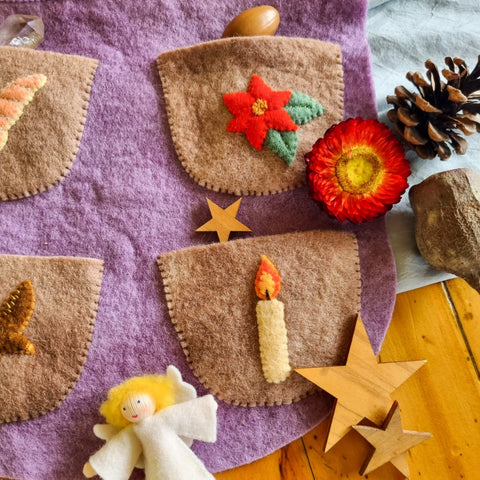 pockets on a handmade wool felt waldorf advent calendar and small gifts to fit inside them like a small felt angel, dried flower, acorn, and pinecone