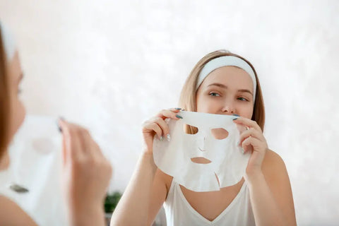 Woman with headband applying face sheet mask in front of mirror