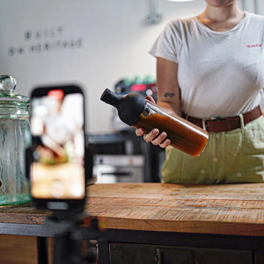 A Coaltown employee shaking a cold brew bottle while being filmed on an iPhone