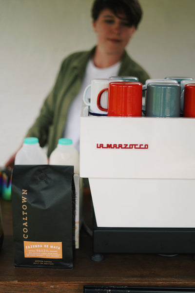 Making coffee with a La Marzocco Linea Mini. Pictured is a coffee grinder, enamel mugs, bottles of milk and a bag of Coaltown Fazenda de Mata coffee. 