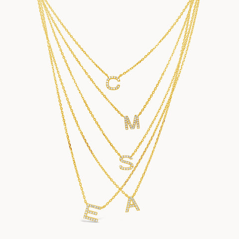 five layered necklaces each with a dainty diamond initial pendant, in yellow gold.