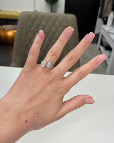 A woman's hand, wearing a platinum engagement ring with rectangular and pear shaped diamonds.