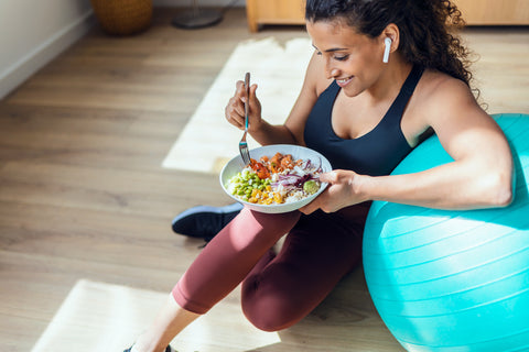 Woman eating a healthy meal after a workout, sitting against an exercise ball