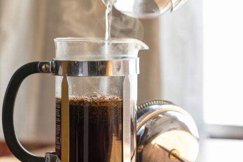 French press on a counter with hot water being poured over coffee grounds