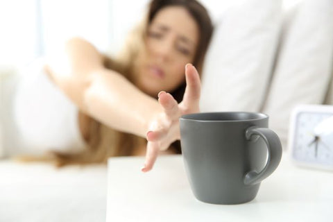 Woman in bed reaching for coffee mug