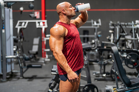 Very muscular man drinks sugar free energy drink during a weightlifting workout at the gym