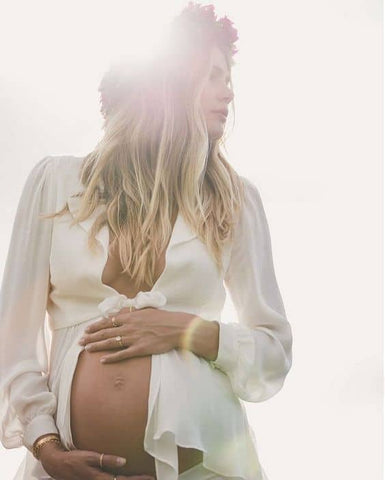 ic:Pregnant mom in a white blouse wearing a flower crown at sunset