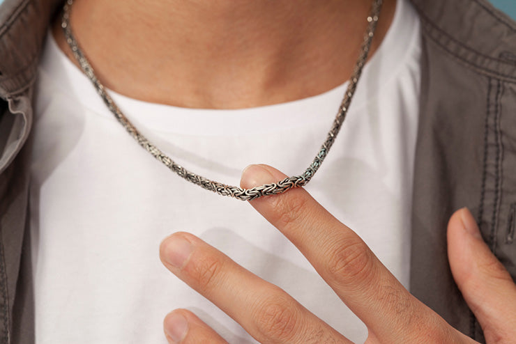a person wearing a silver chain necklace holding it away from their neck with their finger