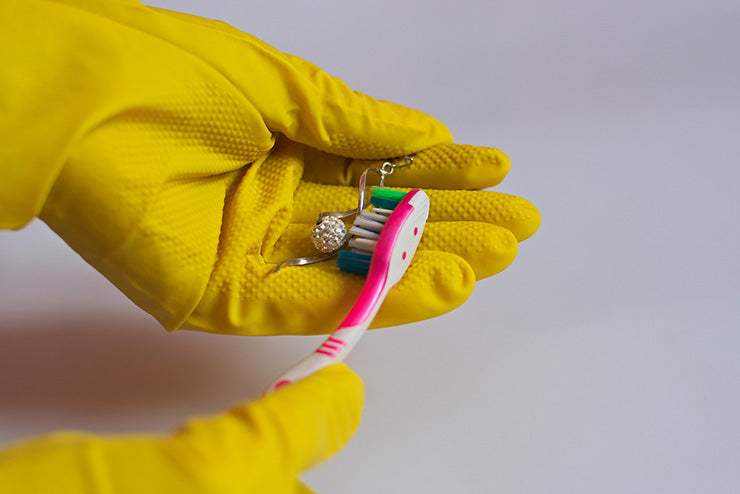 a person wearing rubber gloves cleaning an earring with a toothbrush