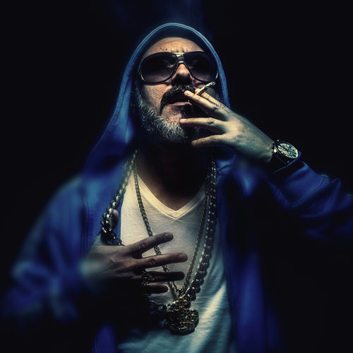 Porträtt av en äldre man som röker en cigarr, bär guldhalsband och blå jacka