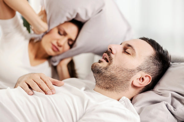 Mattress firmness can influence snoring and sleep apnea shown by a man snoring in bed with an annoyed woman