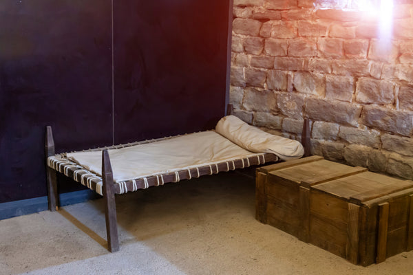 The historical evolution of bedding from ancient civilizations to innerspring mattresses depicted through a bed in the cell of a medieval monastery with poor living conditions and small living space