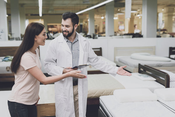 Woman choosing between innerspring and foam mattress for better sleep quality with consultants assistance in store