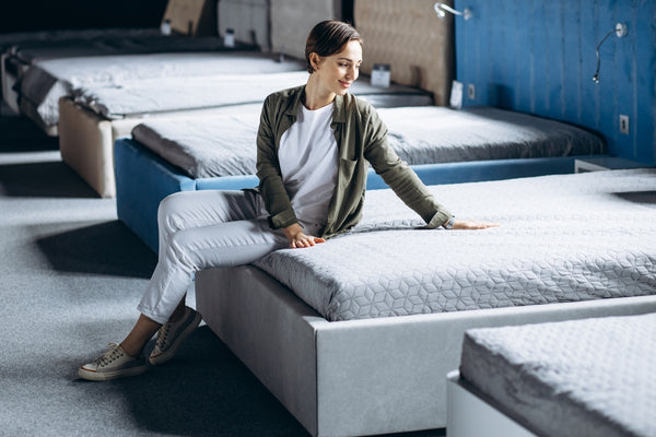 Woman testing foam mattress and innerspring bed to alleviate pressure points in furniture store