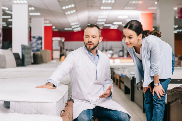 shop assistant in white coat showing female customer mattress in furniture store