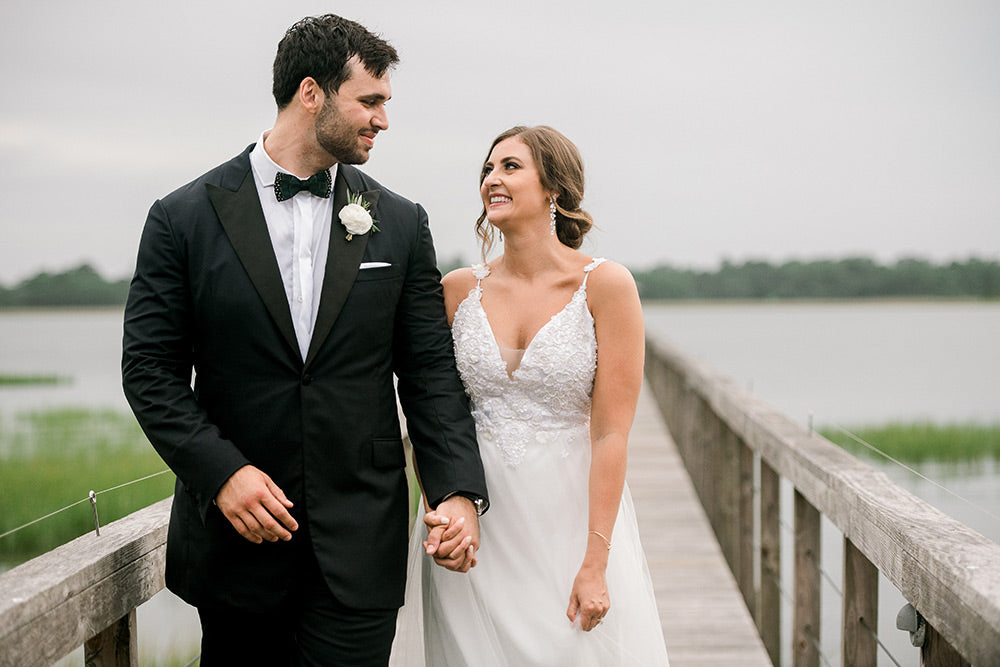 Groom and bride walking on a wooden bridge, looking at each other and holding hands.