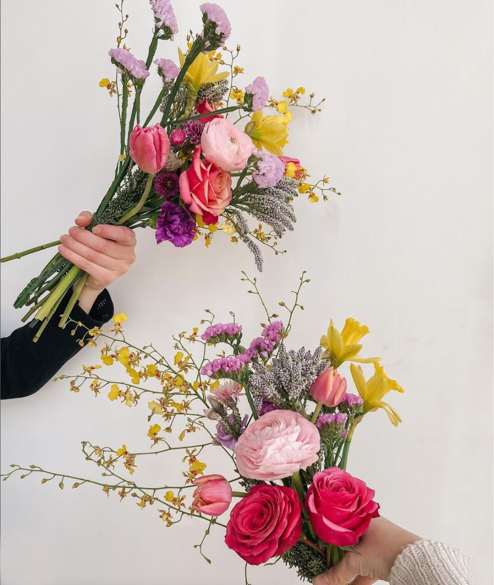 Hands holding 2 spring bouquets against a white wall.