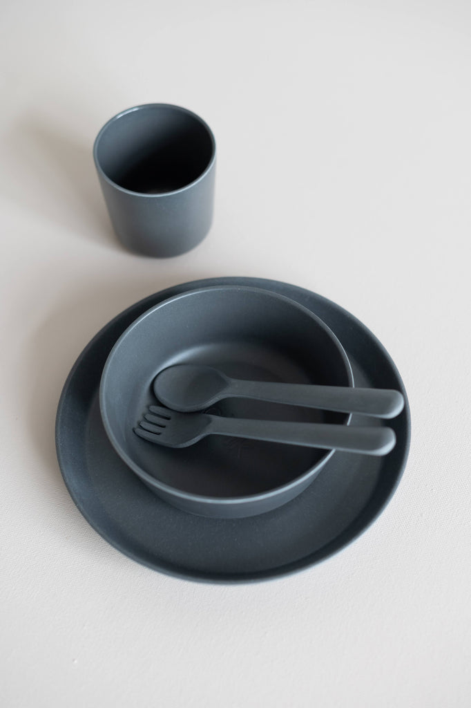 Charcoal bamboo children's dinnerware of a tumbler, bowl, plate and utensils stacked together.