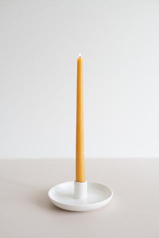 Natural beeswax taper in a white candle holder