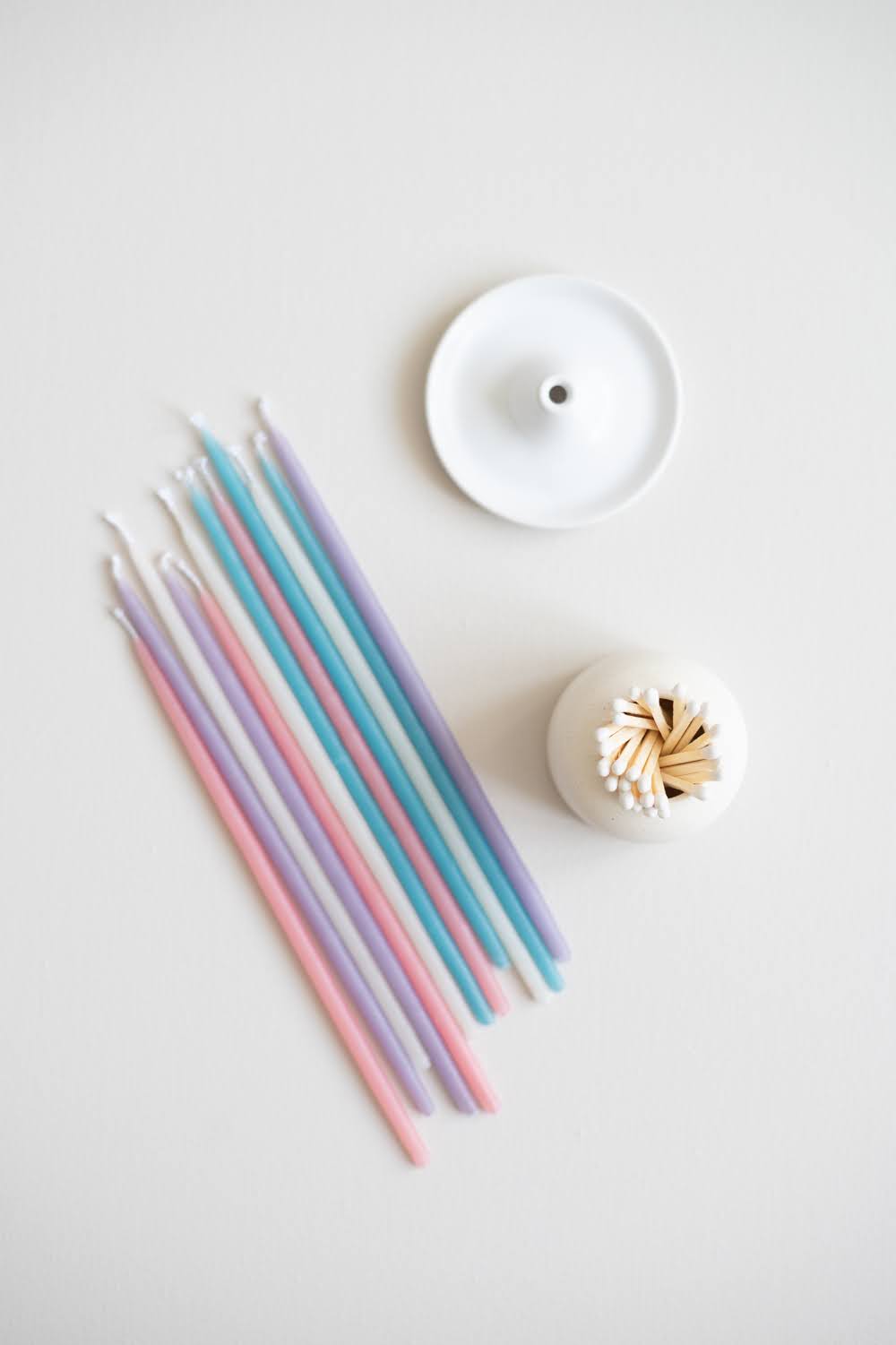 Flat lay of pastel Giving Set with beeswax candles laid out beside a ceramic candle holder and match striker.