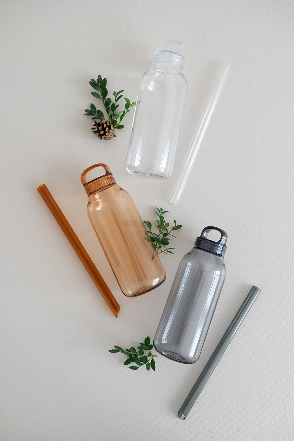 Flat lay of holiday bubble tea gift sets with water bottles, glass bubble tea straws and straw cleaning brushes in clear, amber and smoke colours.