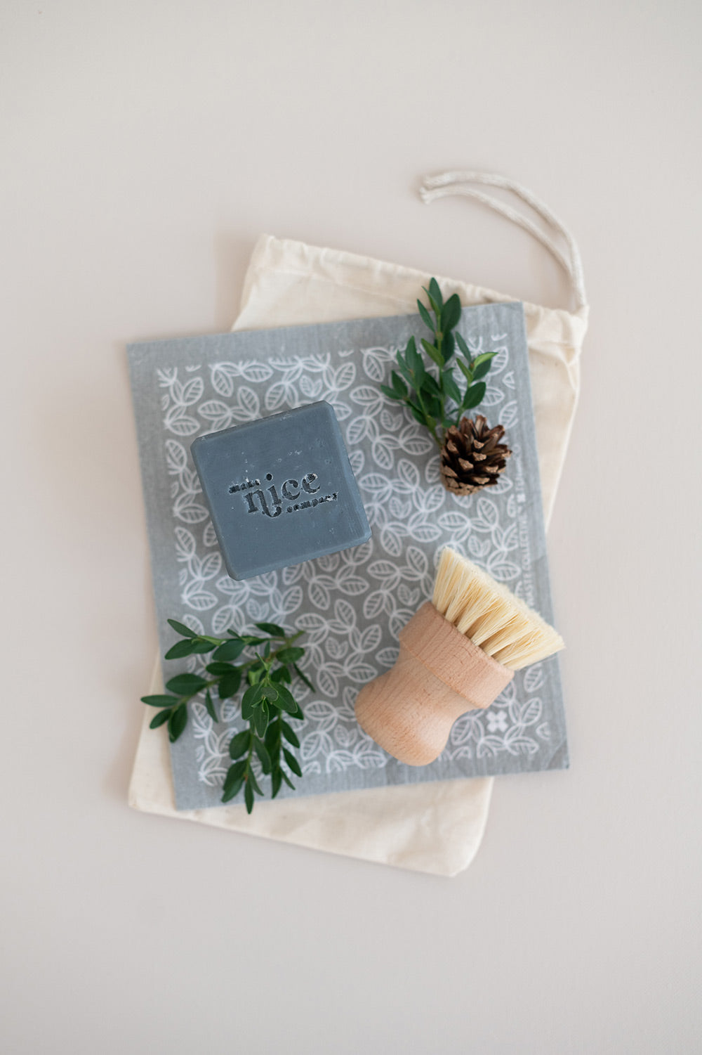 Flat lay of eco-friendly kitchen cleaning gift set with a charcoal solid dish soap, natural dish brush and grey sponge cloth.