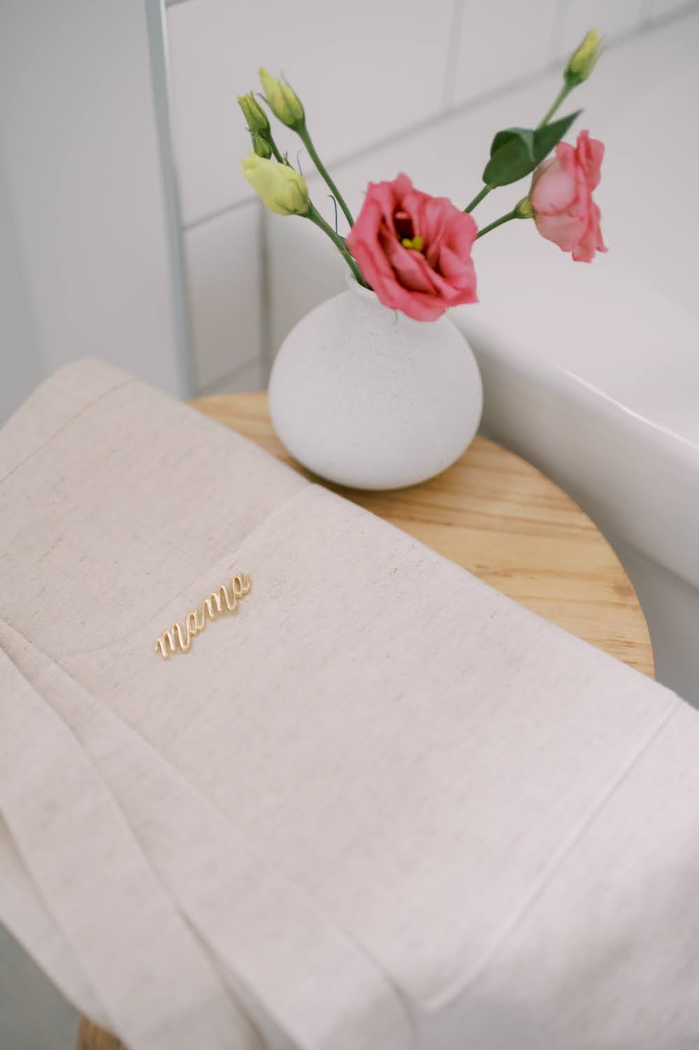 Gather 33 sand apron with mama pin, and a pink lisianthus in a bud round vase on a wooden stool