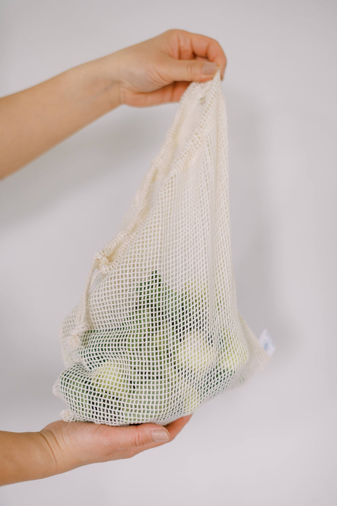 Hand holding a cotton mesh reusable bag with green vegetables