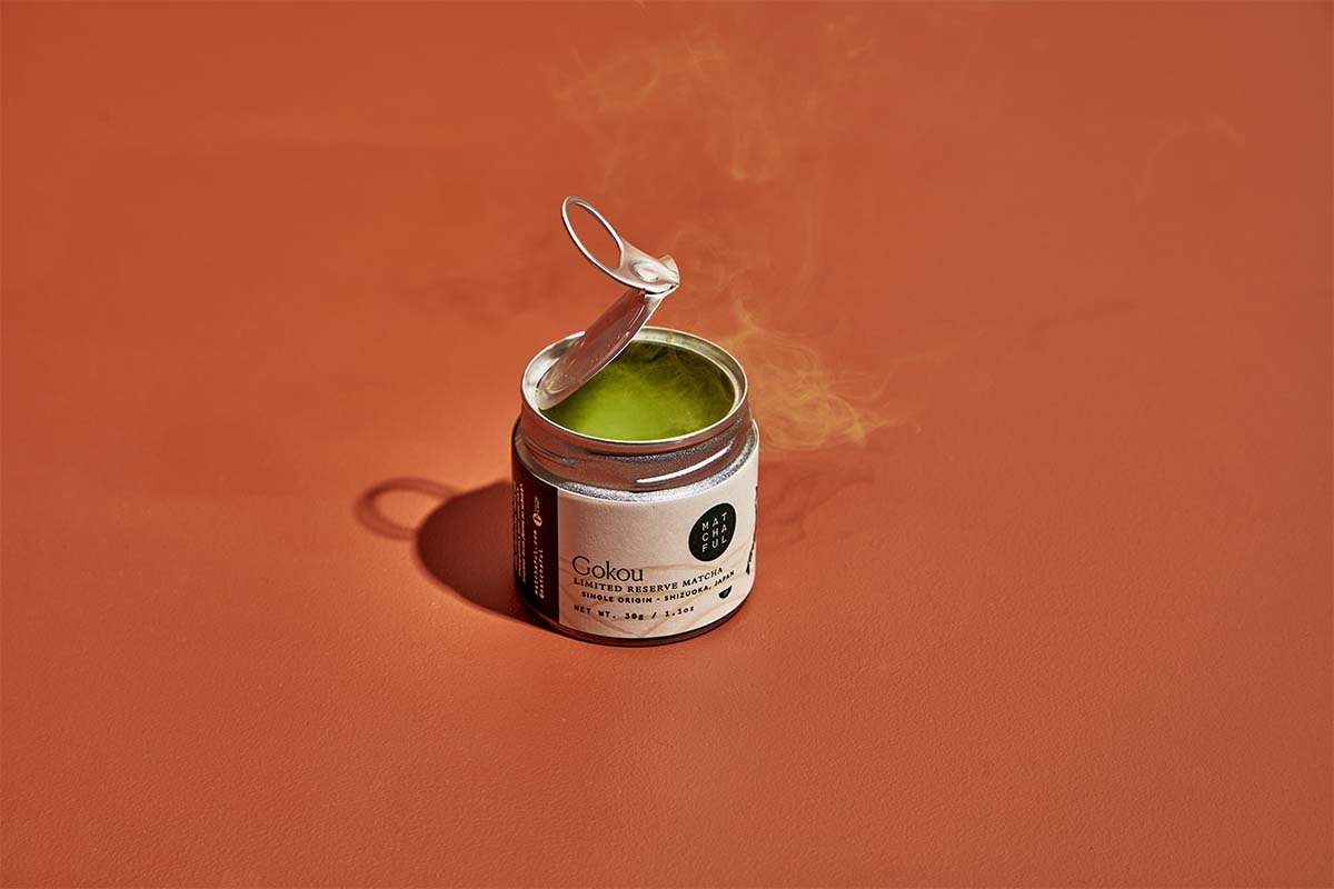 Recently opened tin of Gokou with a swirl of matcha dust against a rust-colored background