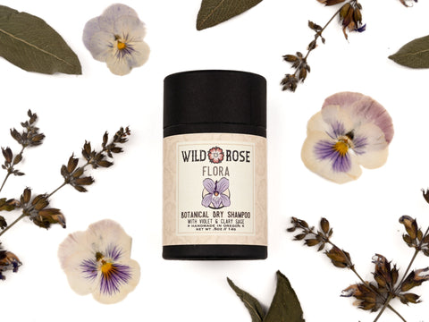 Flora Dry Shampoo in a biodegradable paper tube with dried clary sage, pressed viola flowers and sage leaves surrounding.