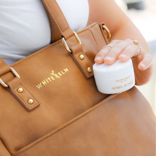 Woman holding a part of her simple skincare routine, Water Balm Moisturizer next to her White Elm bag.