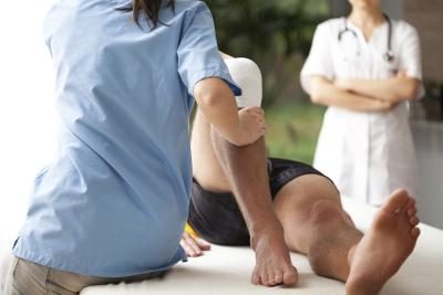 A physical therapist does exercises with a patient's knee