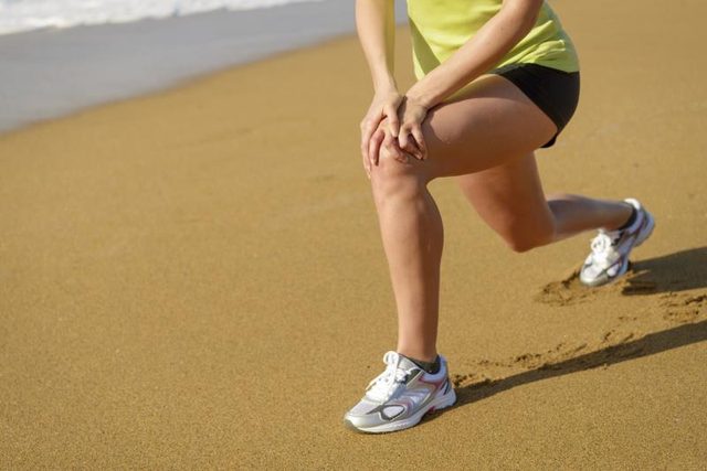 A woman is lunging on the sand.