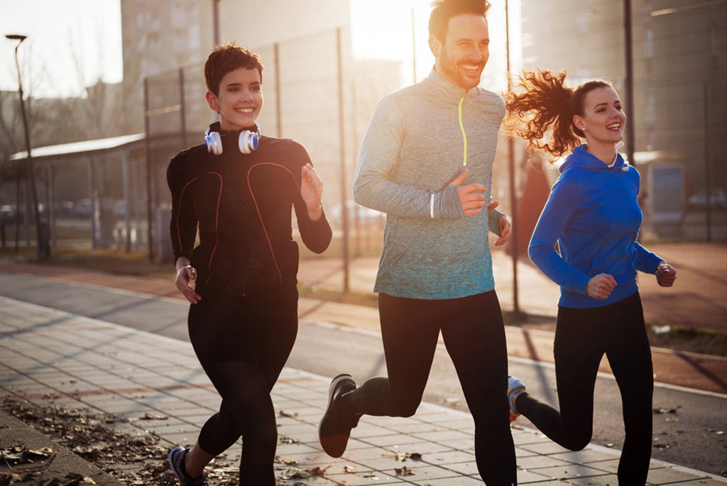 A male and two female friends enjoying exercise outdoors while jogging together on a sidewalk.