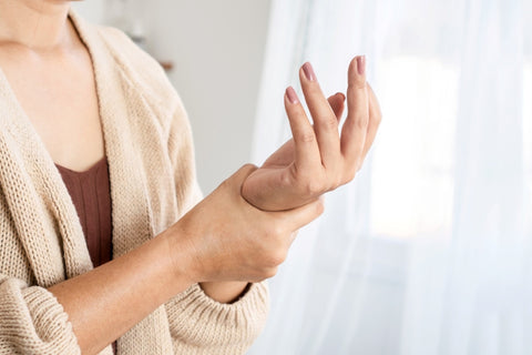 A closeup image of a woman in a cardigan gripping her wrist and open hand. 