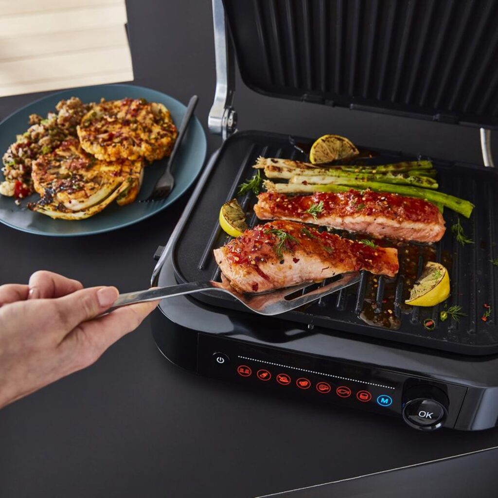 Photograph of a man cooking pork and spring onions on the Swan Stealth Smart Grill next to a plate of vegetarian bean burgers